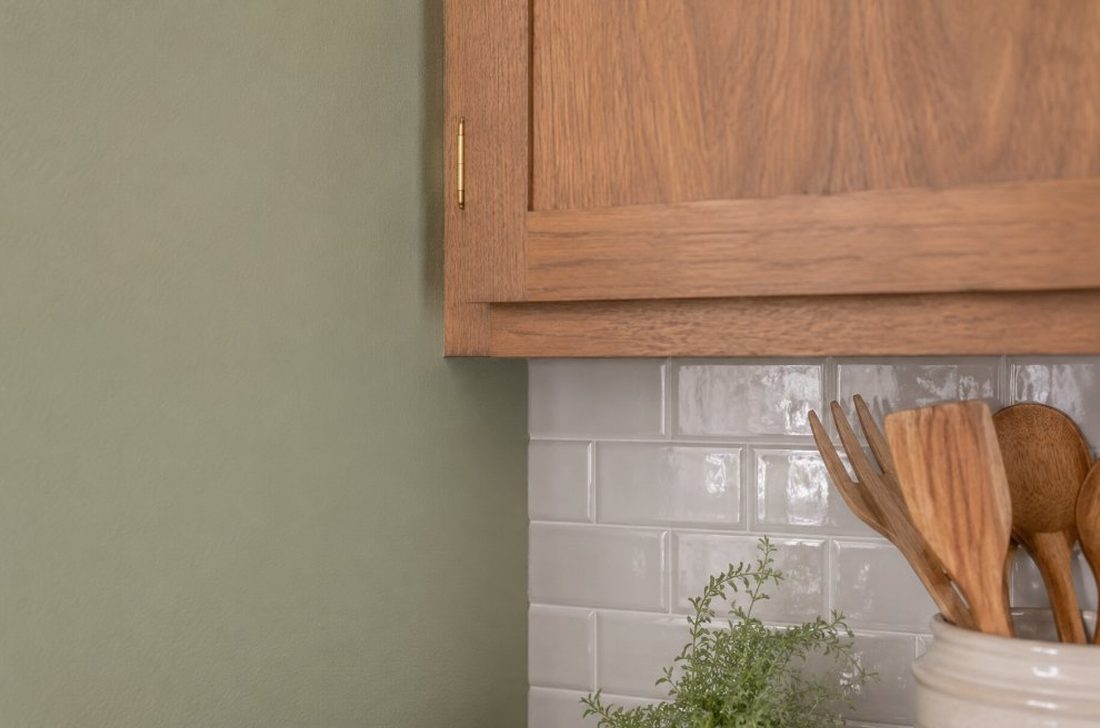 Detalle de pared de cocina pintada en verde salvia junto a muebles de madera